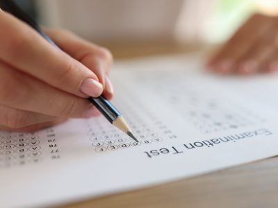 Hand with pencil on examination test paper close up. Education, study, school and university concept. Student taking exam and writing answers.