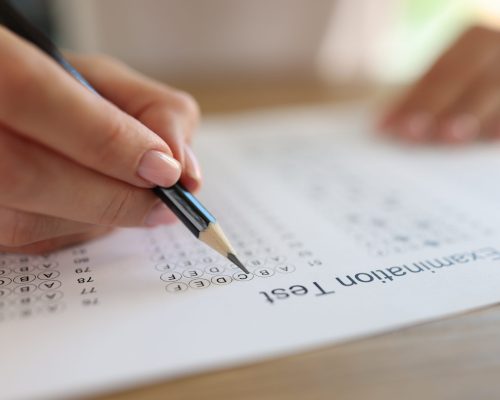 Hand with pencil on examination test paper close up. Education, study, school and university concept. Student taking exam and writing answers.